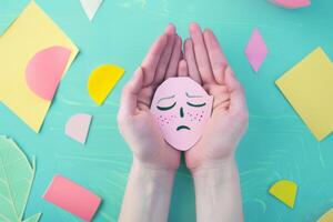 A person is holding a paper cutout of a sad face photo