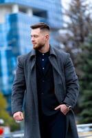 Handsome modern caucasial male model man. fashion businessman wears formal suit and coat outdoor. Blurred background. photo