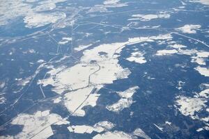 Aerial view from airplane window over clouds top to snow covered rivers, fields and roads photo