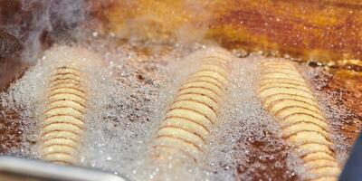 Cooking spiral fried potato in boiling oil, rich in fat and calories fast food, unhealthy delicious photo