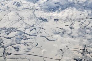 Aerial view over clouds top to snow covered rivers, fields and roads, winter fresh frosty air photo