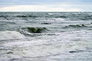 View of blue sea with foaming waves and wooden breakwaters photo