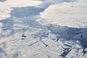 Aerial cloudscape view over clouds top to snow covered rivers, roads, cities and fields, winter air photo