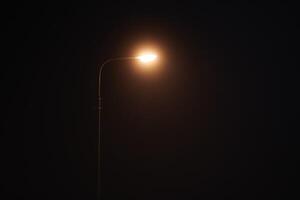 One night lamppost shines with faint mysterious yellow light through evening fog, copy space photo