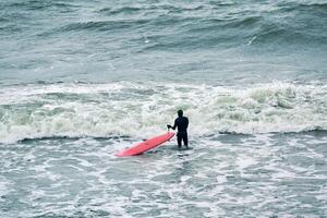 Male surfer in swimsuit in sea with red surfboard photo