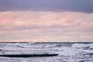 Purple cloudy sky and sea with wooden breakwaters, seascape photo