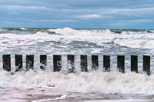 altos rompeolas de madera en olas de mar espumoso y cielo nublado foto