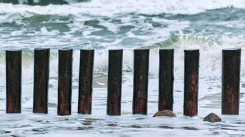 High wooden breakwaters in foaming sea waves photo