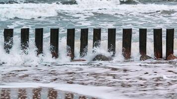 altos rompeolas de madera en las olas del mar espumoso foto