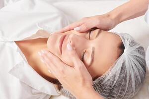 Beautician massages woman face skin after rubbing moisturizing cream for rejuvenation in clinic photo