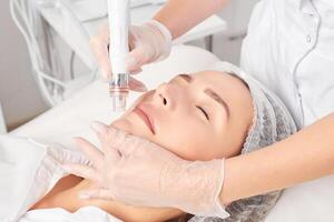 Beautician makes aqua exfoliation for rejuvenation woman face skincare, procedure in beauty salon photo