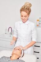Cosmetologist applying cosmetic cream mask on female face for rejuvenation procedure in beauty salon photo