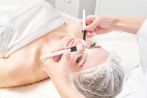 cosmetólogo frotamiento crema con cepillos dentro hembra cara piel para rejuvenecimiento, cosmético procedimiento foto