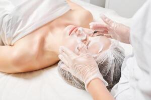 Cosmetologist massages cream mask into woman face skin for rejuvenation, procedure in beauty salon photo