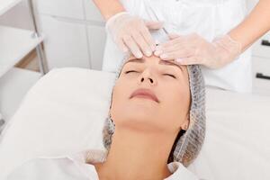 cosmetóloga masajea la piel de la cara de la mujer después de frotar crema hidratante para el rejuvenecimiento en la clínica foto