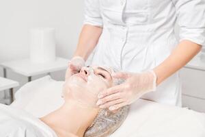 Cosmetologist massages cream mask into woman face skin for rejuvenation, procedure in beauty salon photo