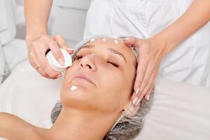 Cosmetologist applying moisturizing cream on woman face for rejuvenation face skin in beauty salon photo