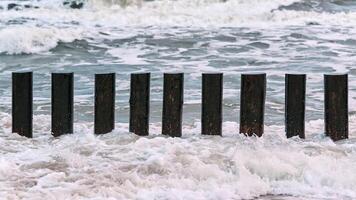 altos rompeolas de madera en las olas del mar espumoso foto