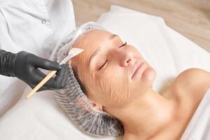 Beautician applies honey mask on woman face for moisturize face skin in beauty spa salon photo