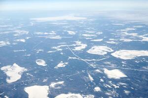 Aerial view from airplane window over clouds top to snow covered rivers, fields and roads photo