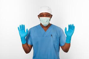 Black surgeon doctor man in blue coat, white cap, surgeon mask, sterile blue gloves white background photo