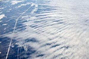 Aerial view from airplane window over clouds top to snow covered rivers, fields and roads photo