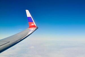 Airplane wing with Russian flag colors over clouds aerial view from aircraft window, parts problem photo