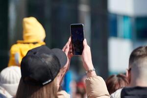 Long haired woman in cap taking photos on phone, back view. Shooting with cell phone camera