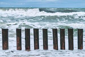 High wooden breakwaters in foaming sea waves and cloudy sky photo