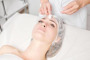 cosmetóloga quitando la máscara de crema facial de la piel de la cara de la mujer con toallitas cosméticas en el salón de belleza foto