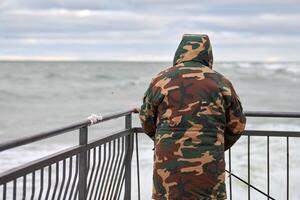 Back view of male fisherman fishing on pier by sea photo