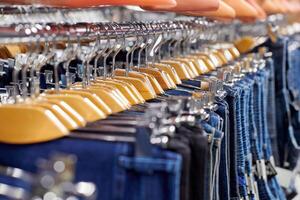 Many denim jeans hanging on wooden hangers, shopping concept photo