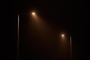 Two night lamppost shines with faint mysterious yellow light through evening fog at quiet night photo