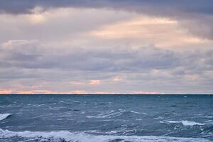 Purple cloudy sky and blue sea with foaming waves, seascape photo