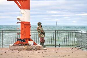 masculino pescador en camuflaje pescar cerca faro foto