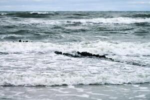 View of blue sea with foaming waves and wooden breakwaters photo