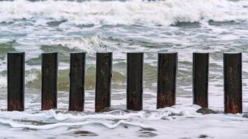 altos rompeolas de madera en las olas del mar espumoso foto