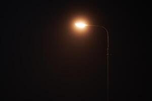 One night lamppost shines with faint mysterious yellow light through evening fog, copy space photo