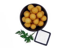 Potato balls in a black plate with sauce and herbs isolated on white background. photo