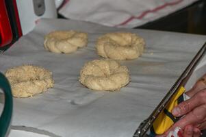 a woman puts a baking sheet with homemade sesame buns in the oven 1 photo