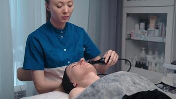 hardware estiramiento facial procedimiento. hardware cosmetología. un hermosa mujer teniendo un linfático drenaje procedimiento hecho en un de cosmetóloga oficina. video