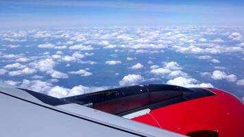 Aerial view of airliner window in the daylight. Aerial view of Cloudscape in dawn through plane window. Side view from the red turbine. Wing of an airplane flying above white clouds against blue sky video