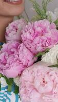 giovane donna riceve mazzo di fiori. contento ragazza Tenere mazzo di peonie. femmina presse un' mazzo di rosa peonie per sua il petto e annusando fiori, lento movimento. internazionale donne giorno video