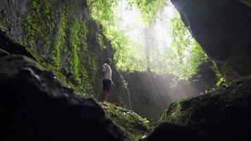 man står på en sten i en djungel grotta med Sol strålar och ljus dimma video