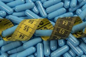 Blue weight loss pills and measuring tape symbolizing slimming photo