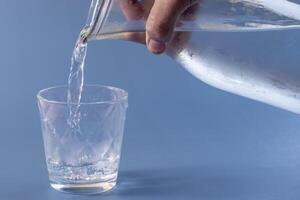 Glass of water being filled on blue background photo