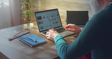 Home Office. A man in glasses with a beard analyzes graphs on the screen of a laptop and tablet video