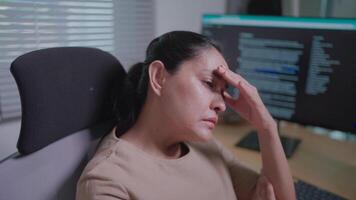 A female app developer is executing code commands on the computer, worried that not completing the task is causing her to stress, pressing her hands to her temples from fatigue from staring at the com video