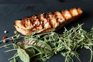 Grilled salmon fish fillet with green salad on the black cutting board, close up photo