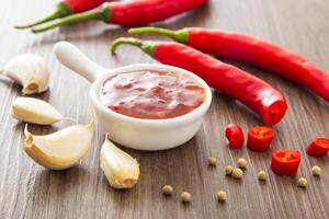 Bowl of hot chili sauce with red peppers on dark wooden background, photo